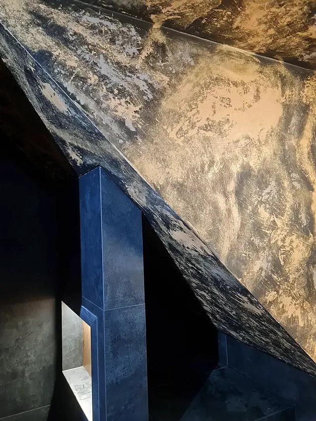 Detail zlato-černé kombi pryskyřičné stěrky s metalickou texturou na šikmém stropě koupelny